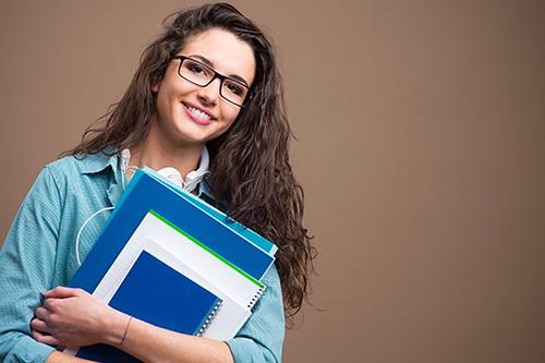 Smiling female college student holding books isolated on a brown background
